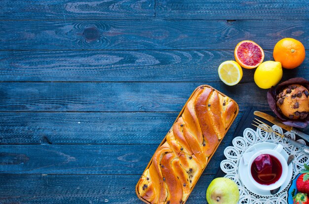 Desayuno con café y té con diferentes pasteles y frutas en una mesa de madera.