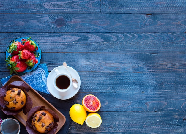 Desayuno con café y té con diferentes pasteles y frutas en una mesa de madera.