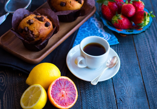 Desayuno con café y té con diferentes pasteles y frutas en una mesa de madera.