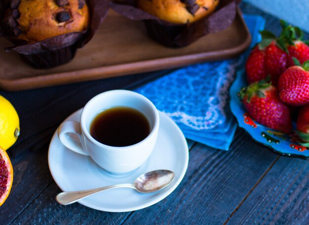 Desayuno con café y té con diferentes pasteles y frutas en una mesa de madera.