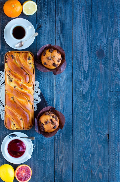 Desayuno con café y té con diferentes pasteles y frutas en una mesa de madera.