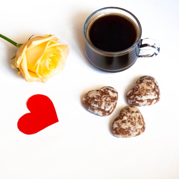 Foto desayuno café, tortas de chocolate en forma de corazones y una rosa amarilla sobre fondo blanco y corazón rojo