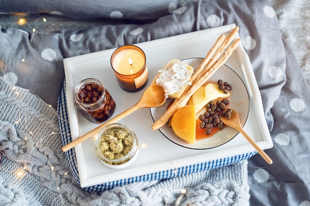 Desayuno en la cama, bandeja con queso, grissini, mermelada de piñas tiernas y vela.