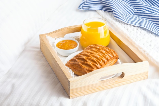 Desayuno en la cama con jugo de naranja en bandeja de madera.