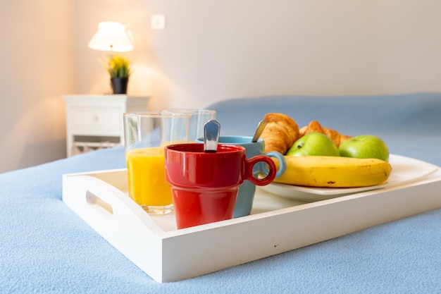 Desayuno en una cama roja despierta saludable con una bandeja con jugos de café y frutas