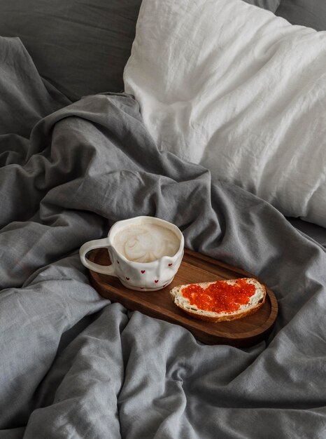 Desayuno en la cama sándwich de caviar rojo y capuchino en una bandeja de madera en la cama Una acogedora mañana perezosa