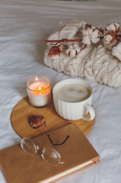 Desayuno en la cama. Taza de café, galletas en forma de corazón, libro, vasos, vela, bandeja de madera. Dia de la mujer. Acogedor.