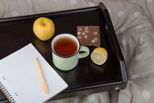 Desayuno en la cama taza de té limón chocolate y cuaderno en bandeja de madera
