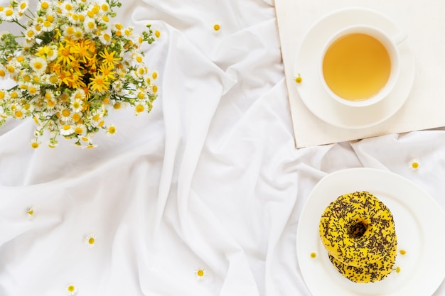 Desayuno en la cama, té con rosquillas amarillas y un ramo de margaritas