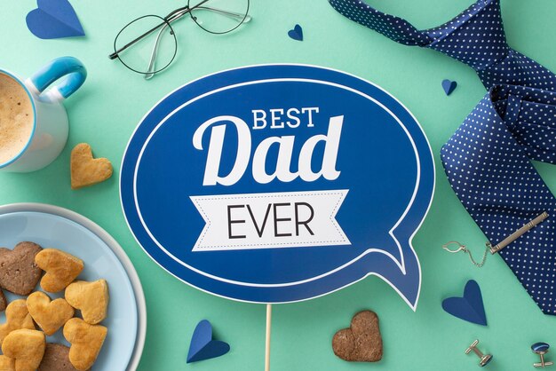 Desayuno casero para papá en el Día del Padre Plato de galletas de vista superior taza de capuchino corazones accesorios corbata gemelos gafas y placa de saludo de moda en fondo azul azulado