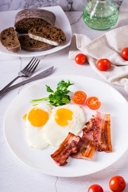 Desayuno casero tocino frito y huevos tomates y verduras en un plato sobre la mesa Vista vertical