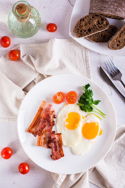 Desayuno casero tocino frito y huevos tomates y verduras en un plato Vista superior y vertical