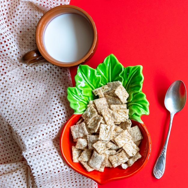 Desayuno de cereales de copos de maíz en un tazón y una taza de leche en rojo