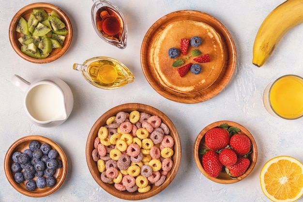 Desayuno con coloridos anillos de cereales, panqueques y jugo de naranja.