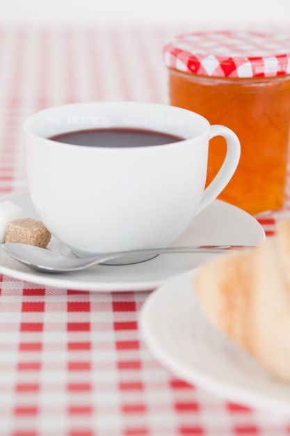 Desayuno continental con croissant, mermelada y café sobre un mantel