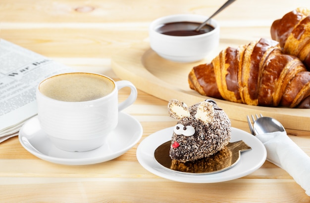 Foto desayuno continental con cruasanes recién hechos de chocolate, un pastel hecho en forma de ratón y café. deliciosos pasteles con café espresso.