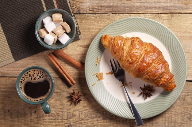 Desayuno con croissant, café, azúcar y especias en una mesa de madera antigua, vista superior