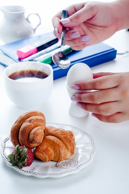 Desayuno croissant y cuaderno sobre una mesa blanca