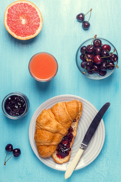 Desayuno con croissant, mermelada, fruta y jugo.