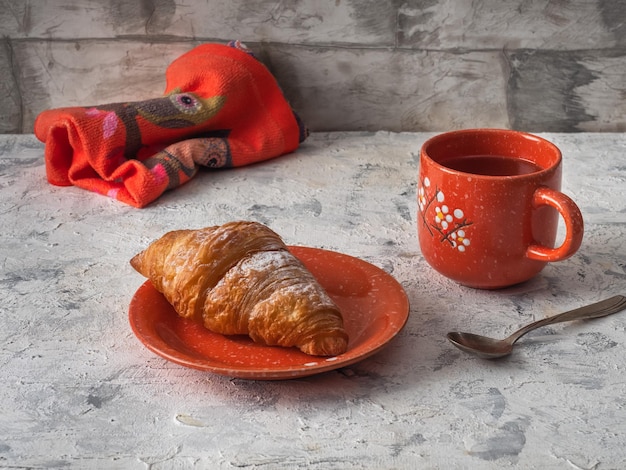 Desayuno con croissant y té en una taza naranja con patrón