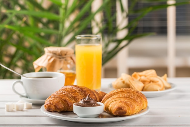 Desayuno con croissants, jugo y café en la mesa.