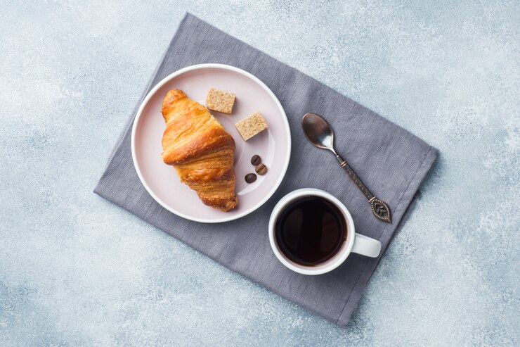 Desayuno cruasanes en un plato y una taza de café sobre la mesa,