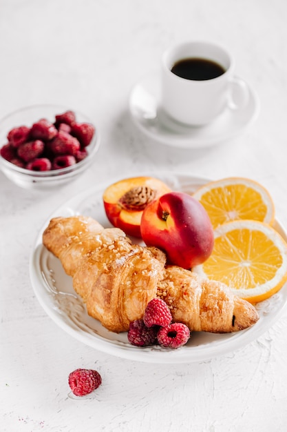 Desayuno con cruasanes, una taza de café, frambuesas y vista superior de jugo de naranja