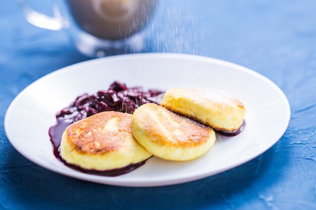 Desayuno y delicioso concepto: panqueques de requesón con mermelada, fondo azul. Espolvorear