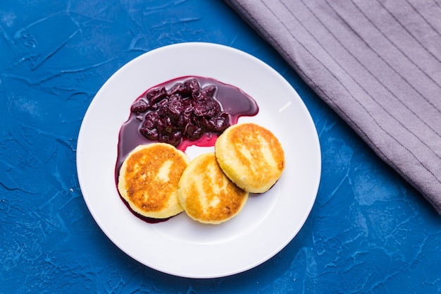 Foto desayuno y delicioso concepto: panqueques de requesón con mermelada, pared azul.