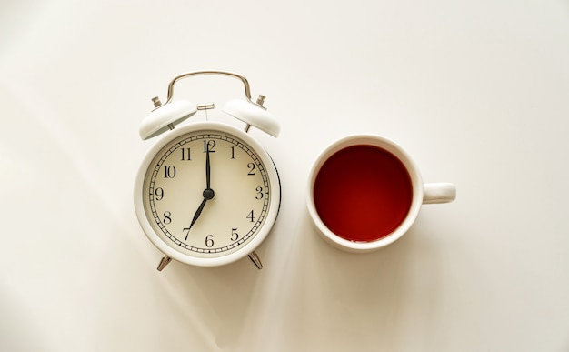 Desayuno delicioso, rápido y sencillo. un despertador y una taza de té en un plato sobre una mesa blanca.