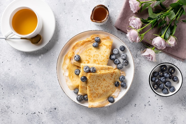 Desayuno delicioso. Tortitas finas, taza de té, bayas y ramo de rosas