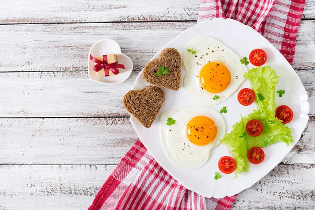 Desayuno en el día de San Valentín: huevos fritos y pan en forma de corazón y verduras frescas. Vista superior