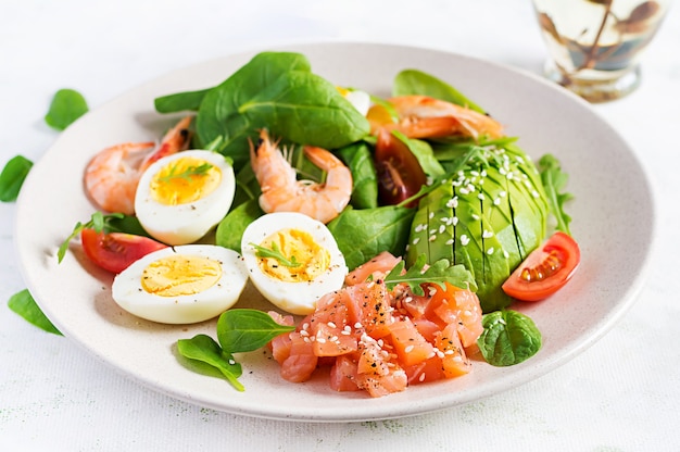 Desayuno de dieta cetogénica. Ensalada de salmón salado con gambas cocidas, gambas, tomates, espinacas, huevos y aguacate.