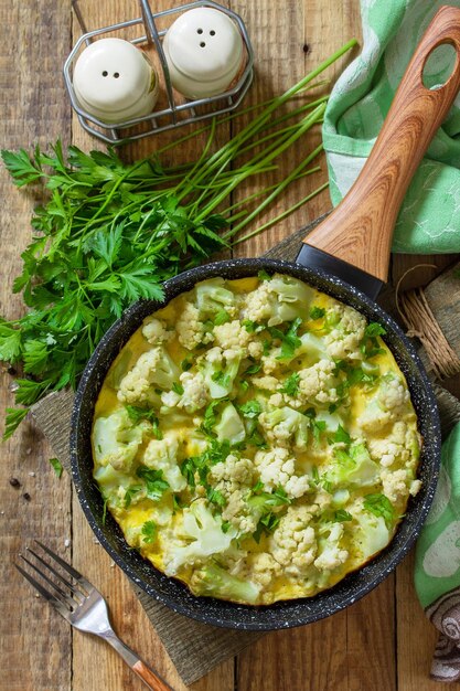 Foto desayuno dietético o almuerzo saludable tortilla de huevo con coliflor en una sartén en una mesa de madera rústica