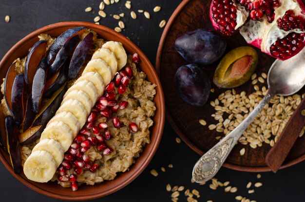 Desayuno dietético de un tazón con gachas de avena, plátano, semillas de granada y ciruela