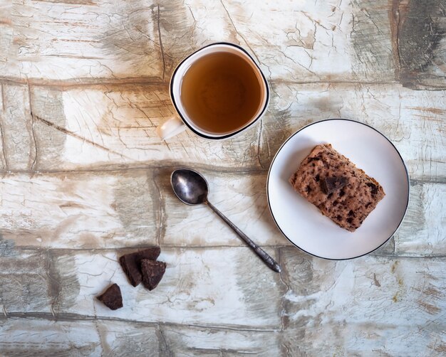 Desayuno dulce con una taza de té y pastel de galletas en una vista superior de plato blanco sobre una mesa de luz