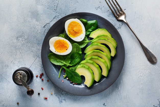 Desayuno de ensalada vegetariana saludable. Hojas de espinaca, tomate, aguacate y huevo cocido en placa gris y hormigón gris antiguo