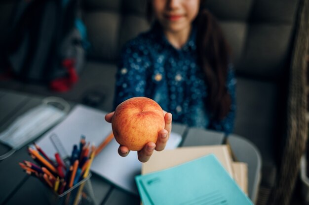 Desayuno escolar saludable, melocotón en manos de una colegiala. merienda durante la tarea