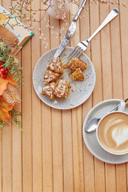 Desayuno estético afuera cortando donas entre decoraciones de otoño Capuchino en taza de cerámica blanca sobre mesa de madera entre flores Almuerzo café