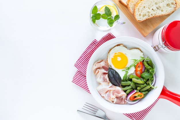 Desayuno europeo: huevo en forma de corazón, tocino, judías verdes sobre una mesa blanca. Enfoque selectivo. Vista desde arriba. Copia espacio