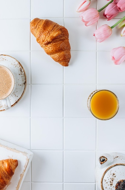 Desayuno francés con croissants, jugo de naranja y café con tulipanes rosas.