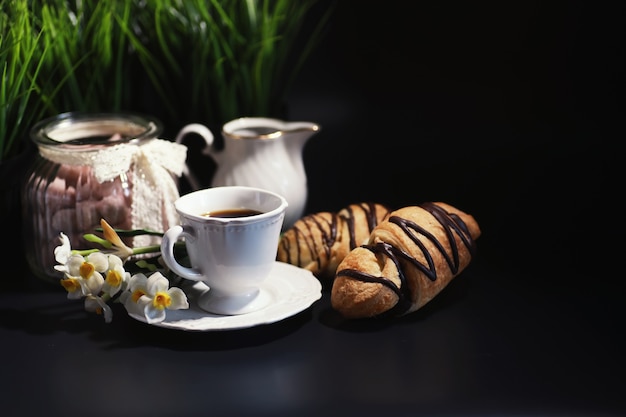 Desayuno francés en la mesa. Croissant de café con chocolate y un decantador con nata. Bollería fresca y café descafeinado.