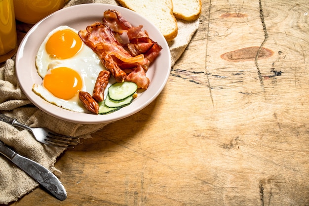 Desayuno fresco. Jugo de naranja con huevos fritos, tocino y rebanadas de pan. Sobre una mesa de madera.