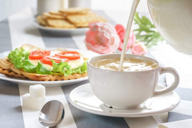 Desayuno fresco y sabroso con un sándwich y té sobre un fondo claro.