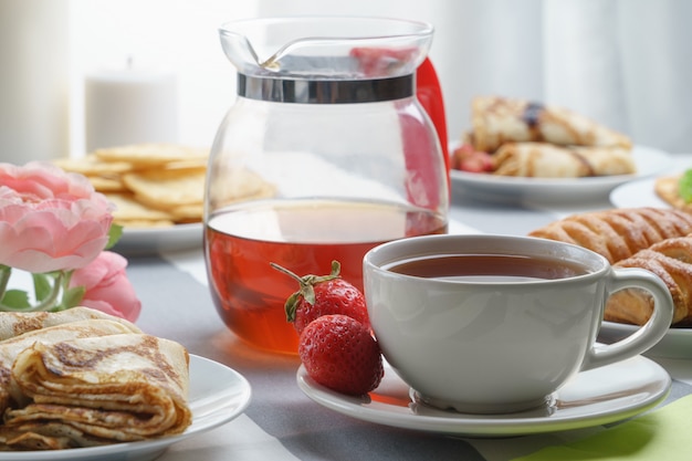 Desayuno fresco, sabroso con té y bollos en un fondo ligero.