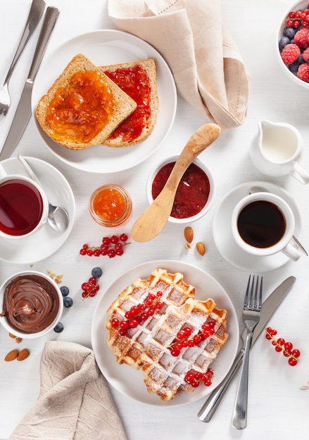 Desayuno con gofres, tostadas, bayas, mermelada, chocolate para untar y café. Vista superior