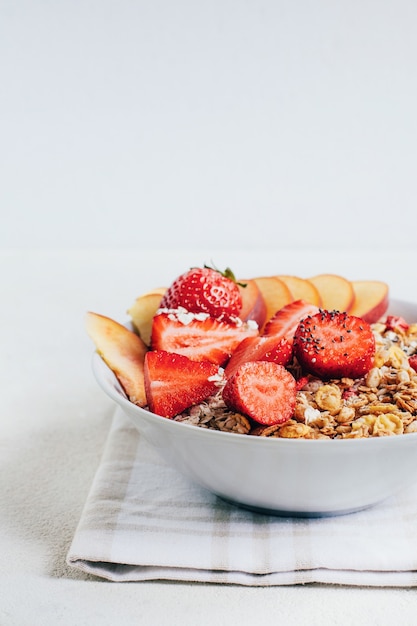 Desayuno granola de cereales de avena con fresas y melocotón en una placa blanca sobre una placa blanca.