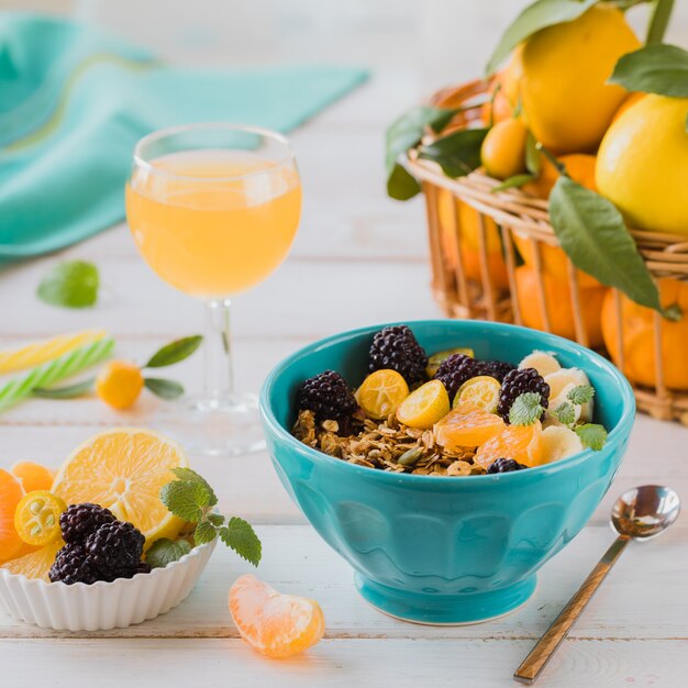 Desayuno de granola, fruta, zumo recién exprimido y té en una mesa blanca.