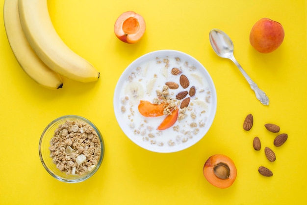 Desayuno de granola con frutas de leche y almendras en el tazón blanco sobre fondo amarillo Vista superior Primer plano