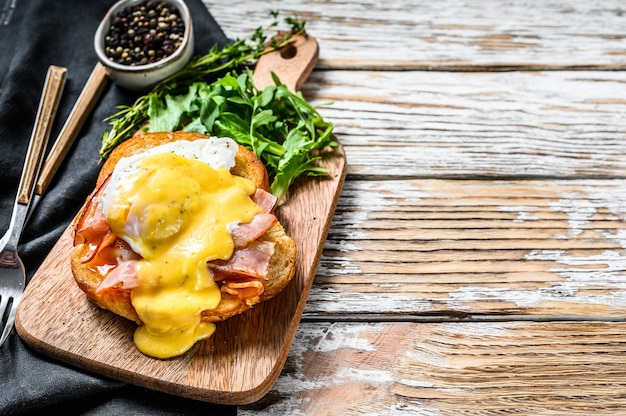 Desayuno hamburguesa con tocino, huevo Benedicto, salsa holandesa en bollo de brioche. Decorar con ensalada de rúcula. Fondo blanco.